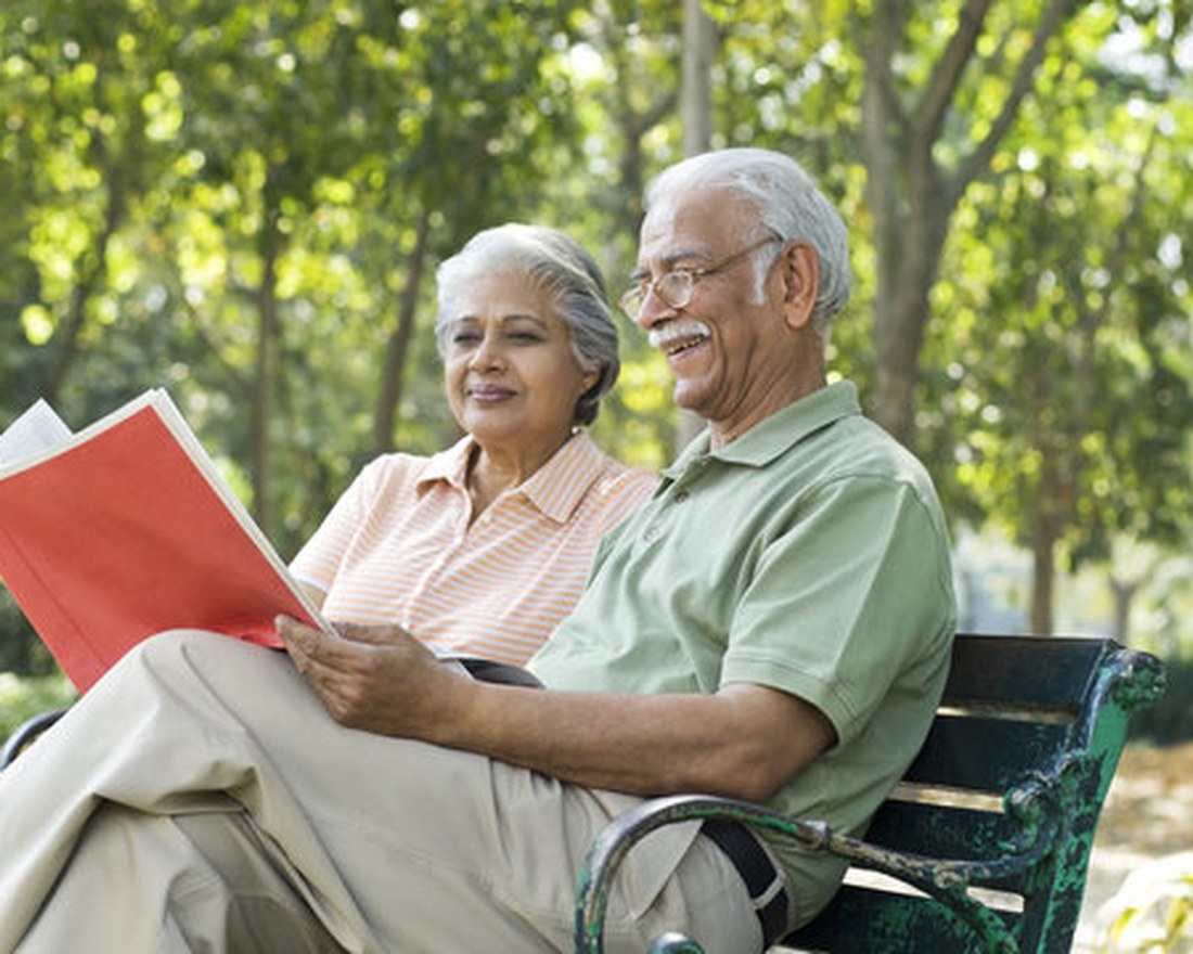 Elderly couple sitting on a park bench, reading a book together